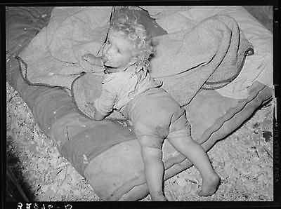 child of white migrant strawberry picker on bed in tent